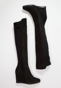 Zwarte over-de-knie sleehakken gemaakt van zacht suède, met een ritssluiting aan de zijkant, een ronde neus en een geribbelde sleehak.