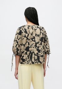 Czarna i beżowa kwiecista bluzka z marszczonym dekoltem, bufkami na rękawach oraz wiązaniami przy mankietach. Gładka faktura materiału, krótki krój.