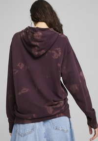Felpa bordeaux con una texture morbida, dotata di cappuccio e motivo tie-dye irregolare di un marrone chiaro. Vestibilità ampia con maniche lunghe.