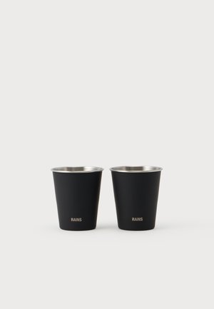 Dos tazas de metal negro mate con bordes plateados y la palabra RAINS impresa en dorado cerca de la base, colocadas una al lado de la otra sobre un fondo blanco.