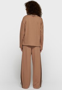 Sweatshirt en coton marron à coupe décontractée avec ourlet côtelé, associé à un pantalon marron à jambes larges avec des accents de bandes latérales.