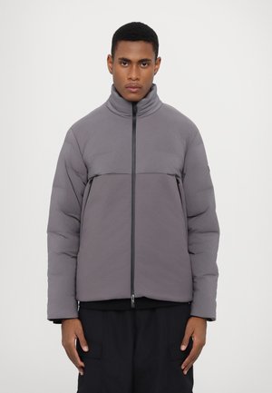 Veste en duvet grise avec col haut, fermeture éclair à l'avant et manches côtelées. Présente une couture horizontale contrastante et une texture douce.