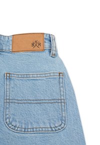 Ljusblå denimjeans med en tan läderpatch som har en präglad logotyp och korskonstruktion. Inkluderar en bakficka med bruna stygn.