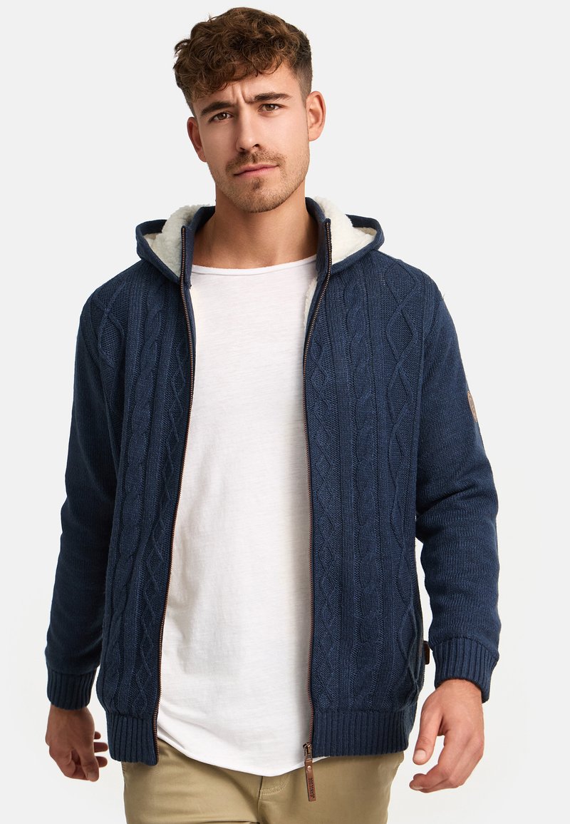 Mørkeblå kabelstrikket hættetrøje med en shearling-foring, lynlås foran, ribbede manchetter og et logo-patch på ærmet.