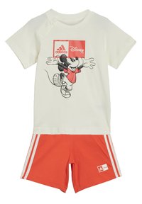 T-shirt chiara in cotone con una grafica di Topolino, abbinata a pantaloni corti arancioni con strisce bianche e logo Adidas. Materiale morbido in cotone.