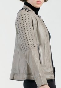 Hellgraue Lederjacke mit Nietenakzenten auf den Schultern, einem Reißverschluss und einer glatten Textur mit einer taillierten Passform.