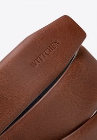 Hnědý kožený opasek s texturovaným povrchem a vyraženým logem "WITTCHEN". Má elegantní stříbrnou sponu a moderní design.
