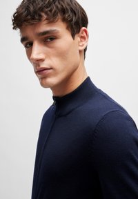Navy blue, knit sweater with a high collar and a short zipper. Features a fitted design and ribbed detailing along the cuffs.