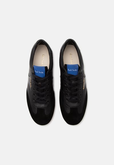 Paire de baskets noires à lacets avec étiquettes bleues sur la languette et marquage doré « Paul Smith » sur les côtés et les semelles intérieures, vues de dessus sur fond blanc.