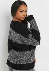 Schwarzer und grauer Kabelstrickpullover mit gestreiften Mustern, ausgestattet mit ribbelten Ärmelbündchen und Saum sowie einem lockeren Schnitt. Die strukturierte Wolle verleiht Tiefe.