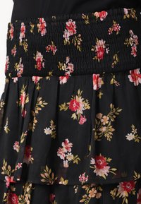 Svart blomstret skjørt med strikket midje, flytende lagdelt design og små røde, rosa og gull blomstermønstre på et gjennomsiktig stoff.