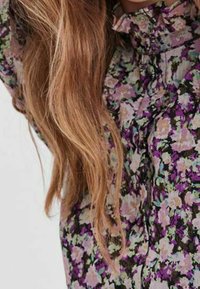 Kukkakuosinen pusero, jossa on violetti, vihreä ja valkoinen kuvio. Kevyt kangas, jossa röyhelökaulus ja löysä istuvuus. Pehmeä koostumus.