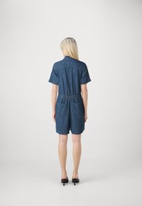 Denim jumpsuit med korte ermer, elastisk midje, to baklommer og krage. Materialet er en middels blå denim.
