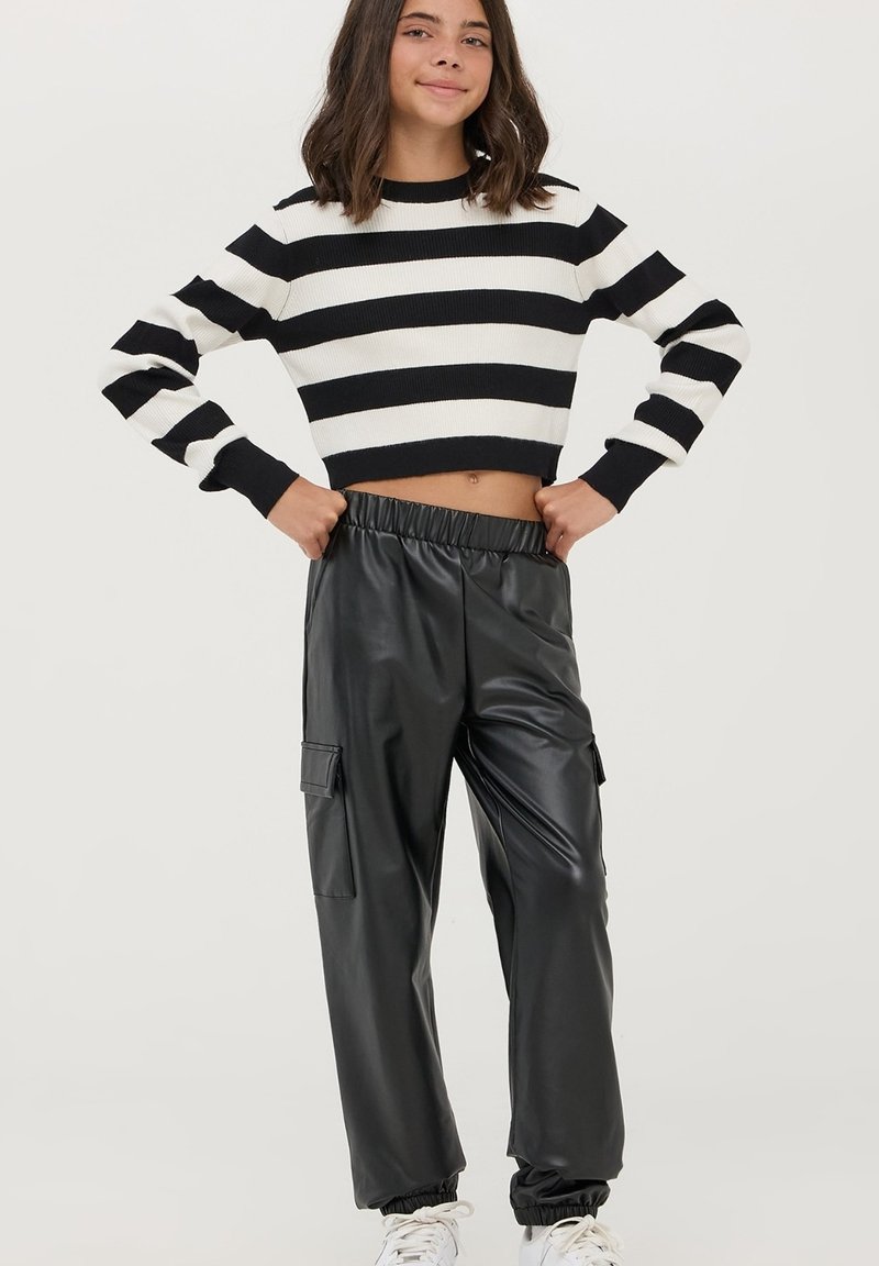 Maglione cropped a righe bianche e nere con maniche lunghe abbinato a pantaloni cargo neri lucidi con vita elasticizzata e tasche laterali.