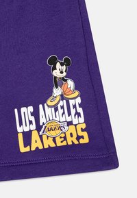 Lila szövet, amelyen Mickey Mouse kosárlabdát tart, és rajta fehér és sárga betűkkel a "LOS ANGELES LAKERS" felirat látható.