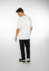 Witte katoenen t-shirt met korte mouwen, ronde halslijn, gedragen met zwarte broek en zwarte sneakers. Glad textuur, comfortabele pasvorm.