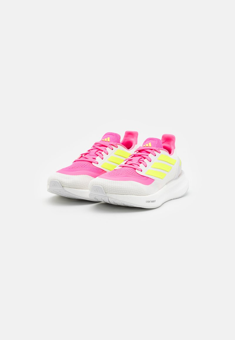 Zapatillas deportivas rosas y blancas con acentos amarillos, material de malla, punta redondeada, suela acolchada y parte superior texturizada. Cordones en rosa a juego.