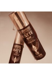 Two bottles of airbrush setting spray with a glossy rose-gold cap, brown matte body, and white text, featuring winged logo and product details.