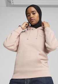 Sudadera con capucha de color rosa claro, hecha de una tela suave, con un bolsillo frontal, puños acanalados y una pequeña etiqueta con logo en el pecho.