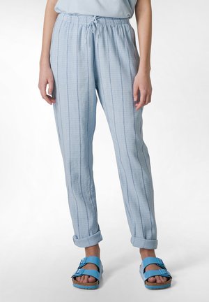 Lichtblauwe, lichte, gestreepte broek met een elastische tailleband. Opgerolde manchetten en een gladde textuur. Draagt met blauwe sandaaltjes.