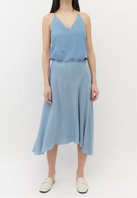 Robe sans manches bleu clair avec un décolleté en V et une jupe asymétrique fluide en tissu lisse. Portée avec des chaussures blanches à enfiler.