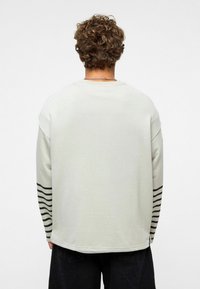 Lichtgrijze sweatshirt met gestreepte zwarte accenten op de mouwen. Heeft een ontspannen pasvorm en een gestructureerde stof. Alleen achterkant zichtbaar.