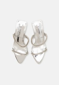 Pantofi cu toc deschis argintii, cu un finisaj metalic strălucitor, având două curele curbate decorate cu mici bijuterii clare și un design cu vârful ascuțit.