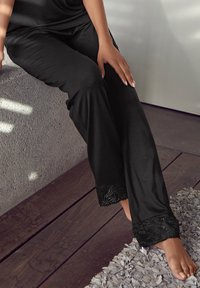 Zwarte pyjamabroek met een losse pasvorm, met delicate kantaccenten aan de zoom. Zachte textuur, wijd model en een eenvoudige bovenkant.