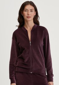 Ritjesjack in diep paars, gemaakt van zachte stof. Voorzien van een ronde kraag, voorzakken en geribbelde manchetten. Eenvoudig en aangesloten ontwerp.