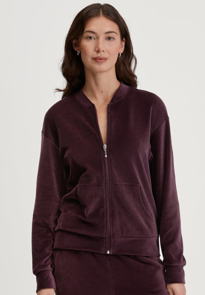 Ritjesjack in diep paars, gemaakt van zachte stof. Voorzien van een ronde kraag, voorzakken en geribbelde manchetten. Eenvoudig en aangesloten ontwerp.