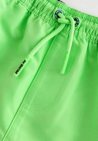 Costumi da bagno verde neon con vita elastica, chiusura con cordoncino e un piccolo logo nero. Tessuto liscio con dettagli di cucitura.