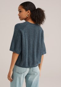 Jersey de punto azul con rayas, de manga corta, escote redondeado y corte relajado. Combinado con unos vaqueros de talle alto en azul claro.