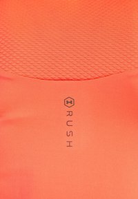 Kirkas oranssi Under Armour -kangas, jossa on kuusikulmion logo ja sana "RUSH" painettuna pystysuoraan tekstuuripaneelin alle.