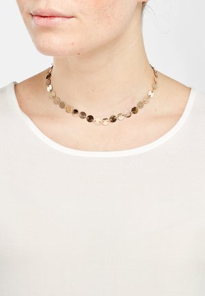 Collana a disco circolare in oro con una serie di dischi piatti e lucenti, creando un aspetto liscio e uniforme, indossata su una maglietta bianca.