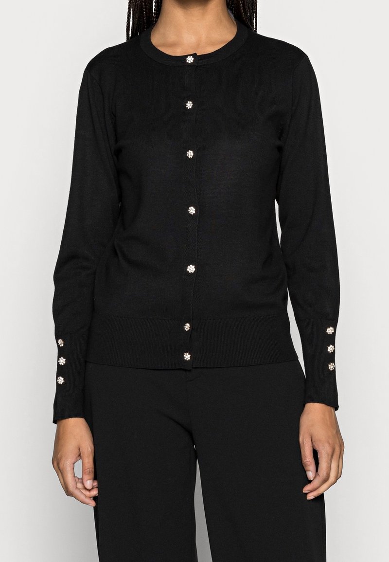 Black cardigan made of ribbed knit fabric, featuring a round neckline and decorative pearl-like buttons along the front and cuffs.