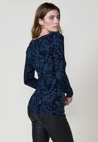 Camiseta de manga larga en azul oscuro con un estampado floral. La tela es suave y tiene un ligero brillo. Presenta un escote redondeado y una silueta ajustada.