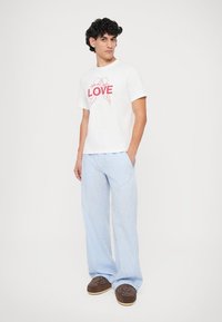 Tricou alb din bumbac cu grafică roz "LOVE", asortat cu pantaloni largi cu dungi albastre deschise și pantofi slip-on maro.