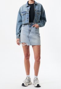 Vaaleansininen farkkutakki, jossa on lyhennetty malli, yhdistettynä vaaleansiniseen farkkuhameeseen, jossa on risat reunat ja hienovarainen repeämä. Valkoiset lenkkarit.