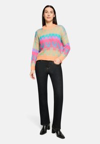 Pull multicolore tricoté avec un motif géométrique en pastels, doté d'un col rond et d'un ourlet côtelé, associé à un jean noir droit.