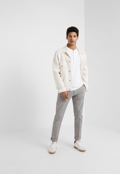 Lys beige denimjakke over en hvit henley-skjorte, kombinert med grå rutete bukser og hvite sneakers med brune såler.