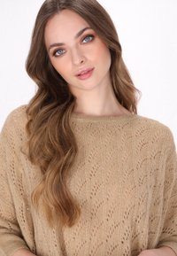 Pulover tricotat de culoare bej deschis, cu un model delicat de frunze, gât larg și croială lejeră, evidențiind o textură fină și o cădere moale.
