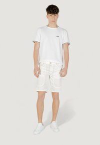 Camiseta blanca de manga corta con un logo negro, combinada con pantalones cortos blancos y zapatillas blancas. Diseño sencillo con acentos en contraste.