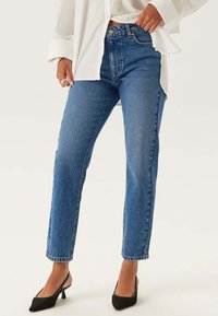 Blå denimjeans med hög midja, rak ben-design och subtila slitningar. Bärs med svarta klackskor och en vit oversized skjorta.