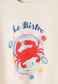 Crabe rouge sur une assiette décorative avec quartiers de citron, coquillages et texte « Le Bistro » au-dessus sur un fond en tissu beige.