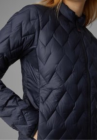Tmavě modrá prošívaná bunda s vysokým límcem, zapínáním na zip, texturovaným vzorem kosočtverců a kontrastními panely po stranách.
