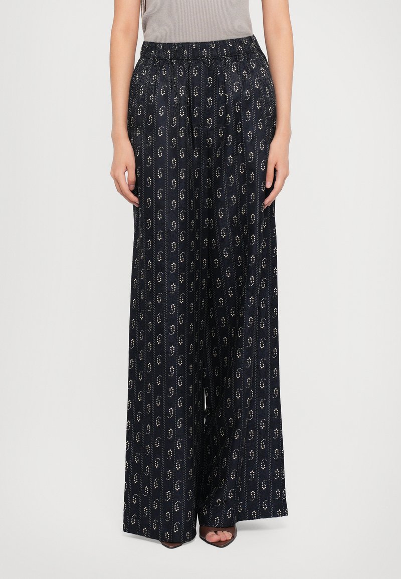 Weite Hosen aus dunkelblauem Stoff mit einem sich wiederholenden goldenen kreisförmigen Muster, einem elastischen Bund und einer glatten Textur.