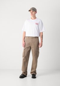 Hvid t-shirt med korte ærmer og rødt "Calvin Klein" logo, parret med beige cargo-bukser med sidelommer. Sorte sko fuldender outfittet.