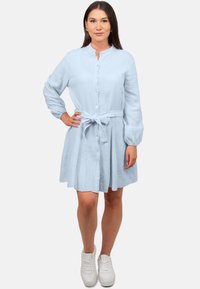 Abito camicia azzurro chiaro realizzato in tessuto testurizzato, con cintura in vita, maniche arricciate e una gonna svasata. Indossato con sneakers bianche.