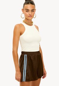 Débardeur blanc côtelé associé à un short de sport marron avec deux rayures verticales bleu clair sur les côtés.