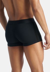 Černé atletické boxerky z hladké látky s širokým pasem a dvěma svislými proužky po stranách.